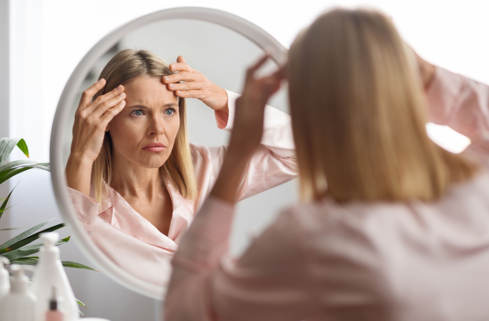 A person looking at herself in a circular mirror, rubbing her forehead and wondering how to get rid of frown lines.