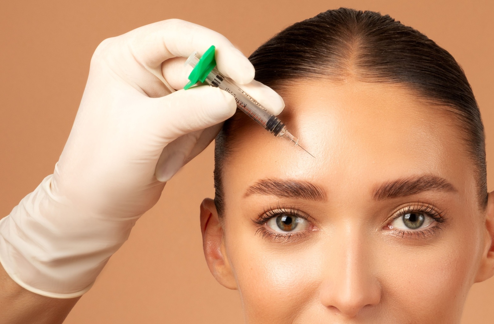 An esthetician holds a needle against a patient's wrinkle-free forehead.