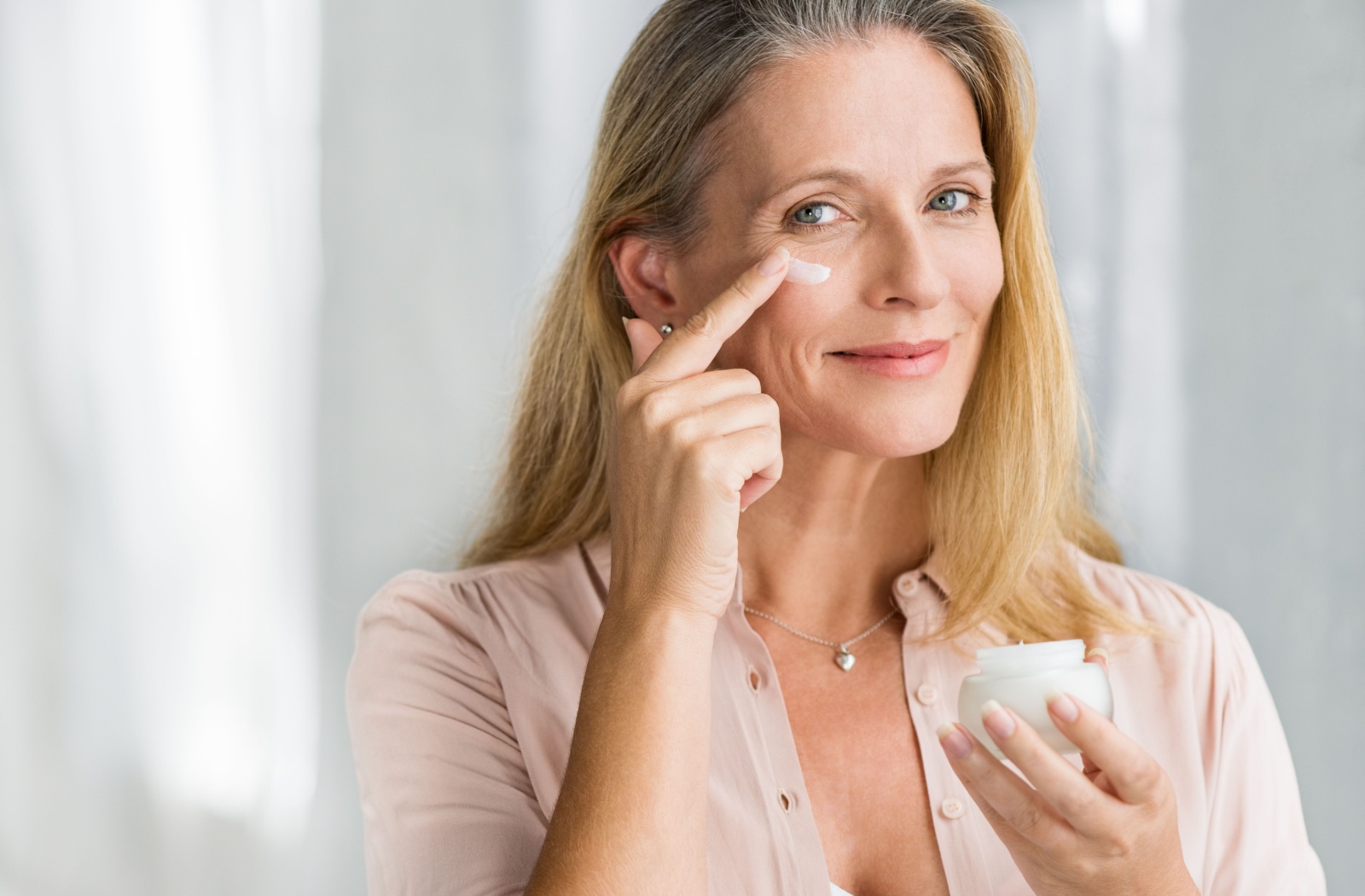 A person with mature skin gently applies eye cream to hydrate their under-eye area.