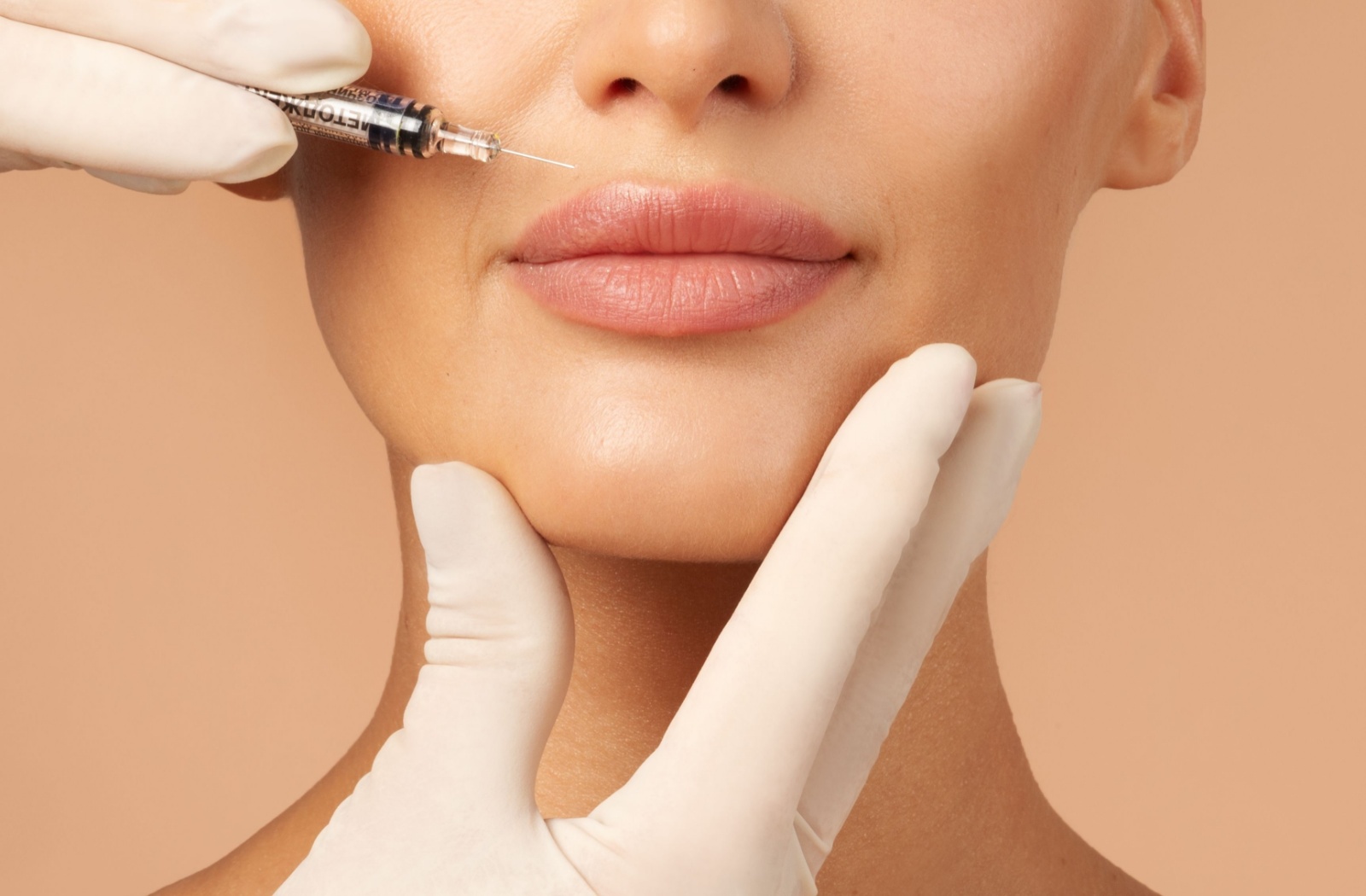 A close-up of a practitioner's gloved hands gently holding a person's face while they inject filler into their lips.