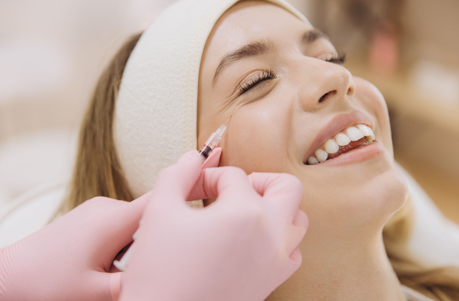 Smiling woman receiving an injection near the outer corner of the eye to treat crow’s feet wrinkles, highlighting a common Botox procedure.