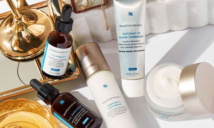 Collection of SkinCeuticals medical grade skincare products including serums, moisturizers, and treatments arranged on white surface with gold decorative lamp.